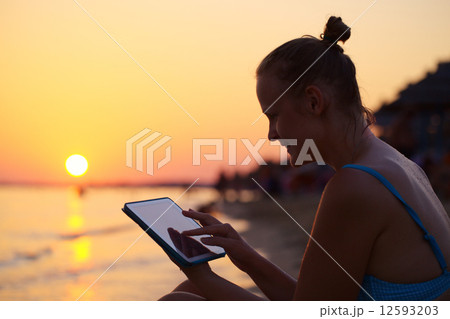 Smiling woman using pad on beach at sunset 12593203