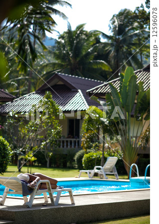 brunette woman sleeps in sunbed near the swimming pool with green palms on background 12596078