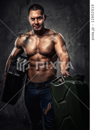 Muscular man with two metal fuel cans indoors Muscular man with two metal fuel cans indoors 12602919