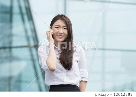 One young chinese office lady making voice call in front of blue glass office building 12612595