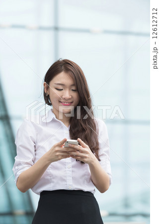One young chinese office lady using smart phone in front of blue glass office building 12612712