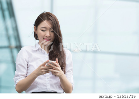 One young chinese office lady using smart phone in front of blue glass office building One young chinese office lady using smart phone in front of blue glass office building 12612719