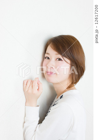 白壁にもたれている笑顔の若い女性 12617200