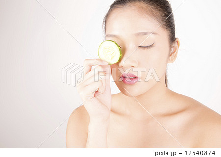 Asian young beautiful woman with flawless complexion holding cucumber slice over eye 12640874