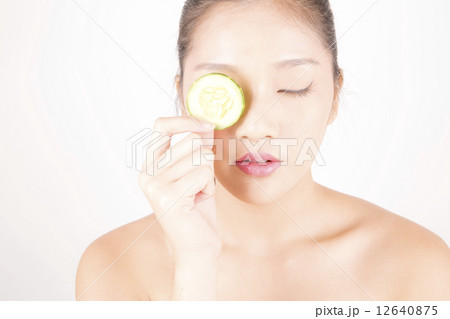 Asian young beautiful woman with flawless complexion holding cucumber slice over eye Asian young beautiful woman with flawless complexion holding cucumber slice over eye 12640875