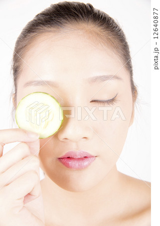 Asian young beautiful woman with flawless complexion holding cucumber slice over eye close up 12640877