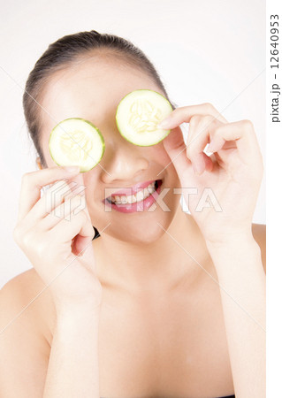 Asian young beautiful smiling woman with flawless complexion holding cucumber slices over eye Asian young beautiful smiling woman with flawless complexion holding cucumber slices over eye 12640953