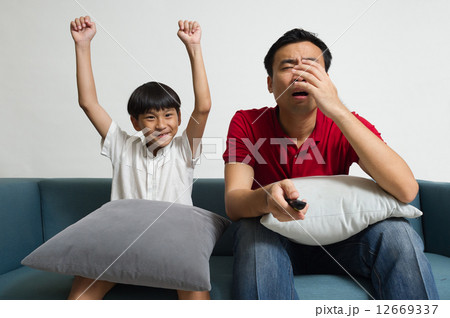 Asian Father and son watching sport supporting different team in the living room 12669337