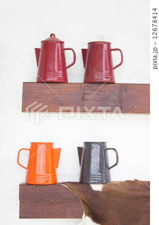 Colorful metal jugs on wooden shelf. 12678414