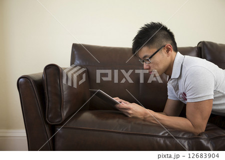 Happy Asian man using digital tablet at home on sofa. 12683904