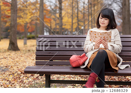 秋の紅葉が綺麗な公園で読書する女性の写真素材