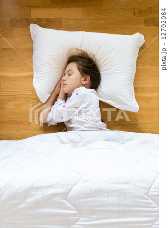 little girl sleeping on wooden floor on white pillow 12702084