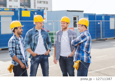 group of smiling builders in hardhats outdoors group of smiling builders in hardhats outdoors 12711387
