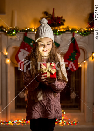 girl in wool sweater and hat looking inside of glowing present b 12736399