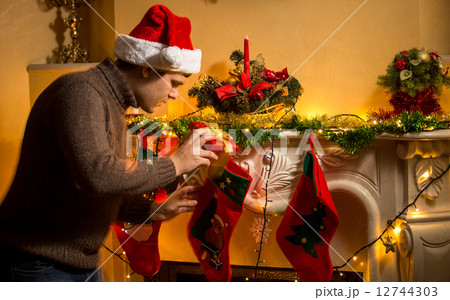 young father putting gifts in Christmas stockings at fireplace young father putting gifts in Christmas stockings at fireplace 12744303
