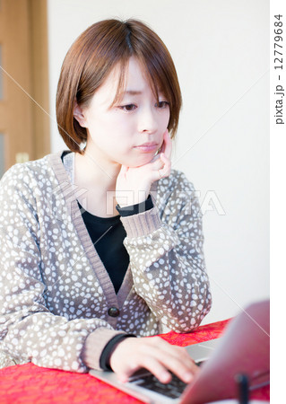 頬づえをつきながらノートパソコンを操作する若い女性 頬づえをつきながらノートパソコンを操作する若い女性 12779684