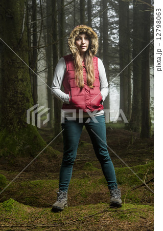 A young woman standing in a forest with her hood up and hands in her pockets. 12798063