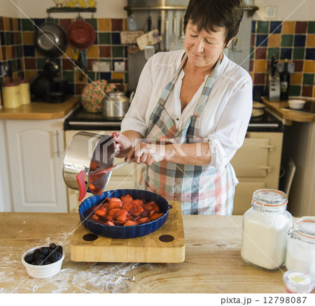 A woman pouring cooked apple and blackberry fruits in to a pie dish. 12798087