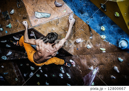 Muscular man practicing rock-climbing on a rock wall indoors 12800667