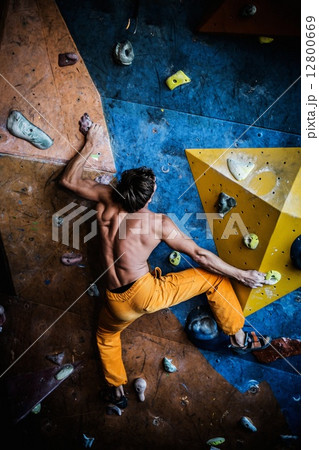 Muscular man practicing rock-climbing on a rock wall indoors 12800669