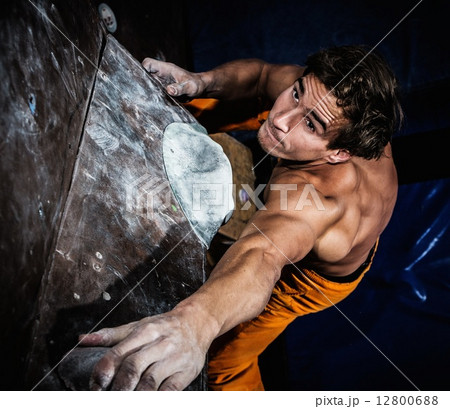 Muscular man practicing rock-climbing on a rock wall indoors 12800688