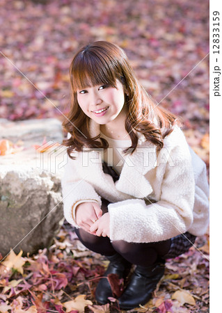 落ち葉の地面にしゃがむ笑顔の若い女性の写真素材