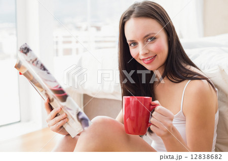 Pretty brunette sitting on floor reading magazine 12838682