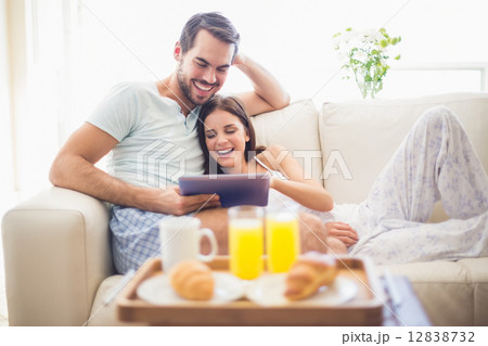 Cute couple relaxing on couch with tablet at breakfast 12838732