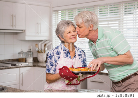 Senior man giving his wife a kiss while taking muffin 12838891