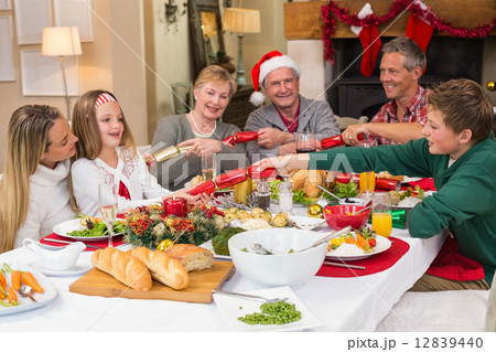 Smiling family pulling christmas crackers at the dinner table Smiling family pulling christmas crackers at the dinner table 12839440