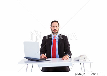 Unsmiling businessman sitting at desk Unsmiling businessman sitting at desk 12841000