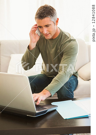 Man on the phone sitting on the couch and using laptop Man on the phone sitting on the couch and using laptop 12841088