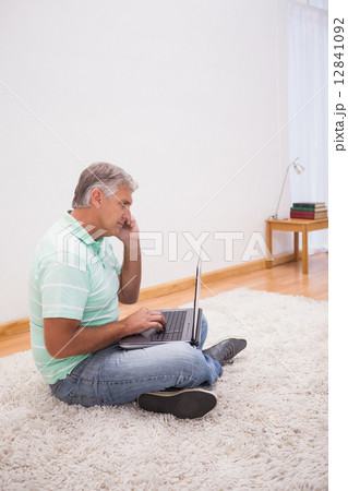 Mature man sitting on rug using laptop Mature man sitting on rug using laptop 12841092