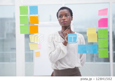 Creative businesswoman looking at sticky notes on window 12841502