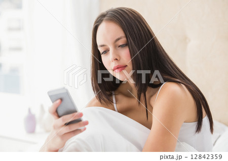 Pretty brunette sending a text on bed Pretty brunette sending a text on bed 12842359