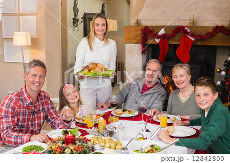 Woman holding turkey roast with family at dining table 12842800