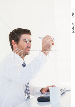 Businessman holding pen up at desk Businessman holding pen up at desk 12843088