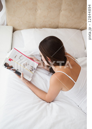 Pretty brunette reading magazine on bed 12844894
