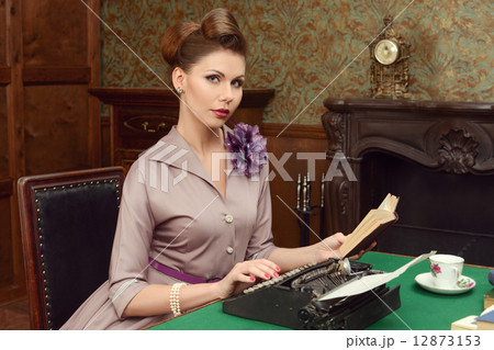 Pin Up beautiful young woman in vintage interior reading a book and prints on an old typewriter 12873153