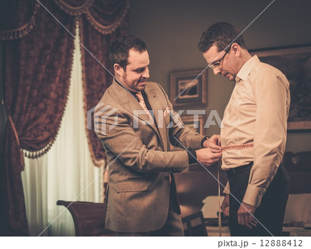 Tailor measuring client for custom made suit tailoring 12888412