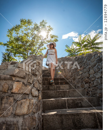 woman in white hat walking down the stone stairs at sunny day 12894779
