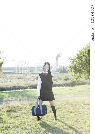 緑を背景に手を振る笑顔の女学生 12934027