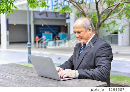 Senior Asian businessman connecting to his business using mobile device at outdoor Senior Asian businessman connecting to his business using mobile device at outdoor 12956874
