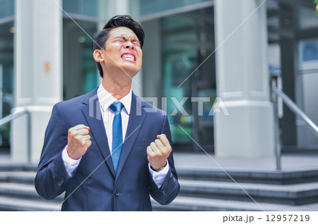 Young Asian expressive businessman in suit and tie clinch his fists in urban setup 12957219