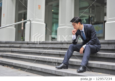 Portrait of a handsome young Asian businessman in suit and tie seating on the stairway pondering  12957234