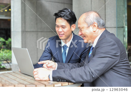 Two Aisan men in suit having discussion in front of a laptop in cafe 12963046