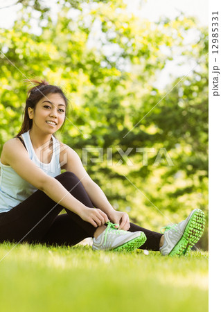 Healthy woman relaxing in park as she ties shoelace Healthy woman relaxing in park as she ties shoelace 12985331