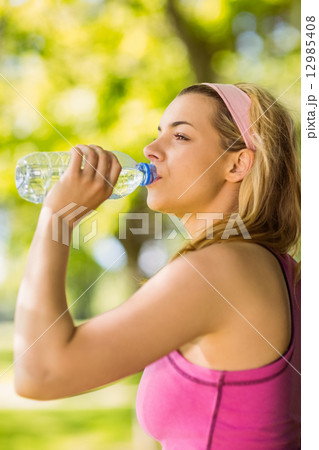 Fit blonde leaning against tree drinking water 12985408