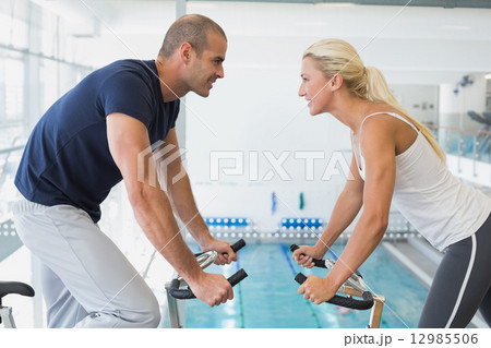 Side view of couple working on exercise bikes at gym Side view of couple working on exercise bikes at gym 12985506