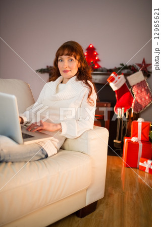 Smiling redhead woman using laptop on couch at christmas 12985621